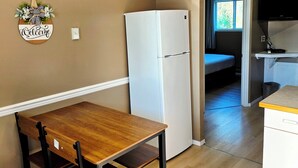 A compact kitchen with a white refrigerator, a wooden dining table with chairs, and a small countertop.