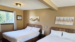 A hotel room with two wooden beds, a large window with a view of trees, and artwork on the walls.