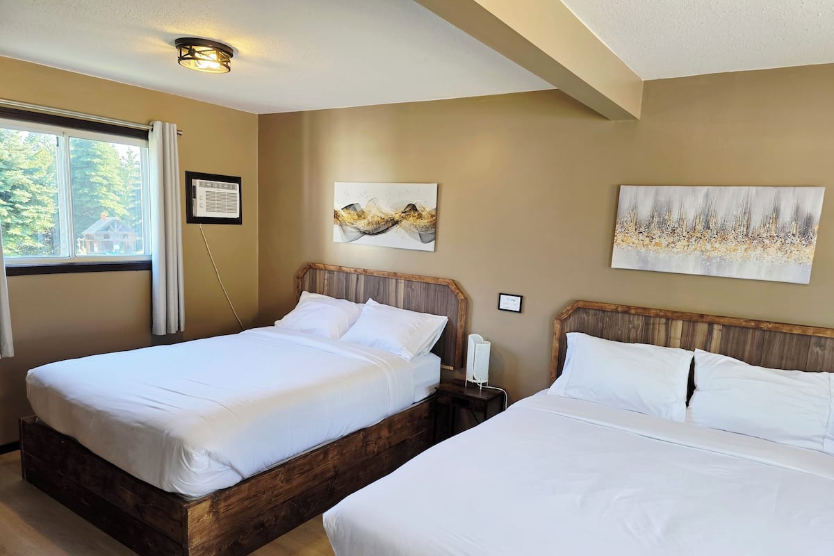 Quarto de hotel com duas camas de madeira, uma janela grande com vista para árvores e obras de arte nas paredes.