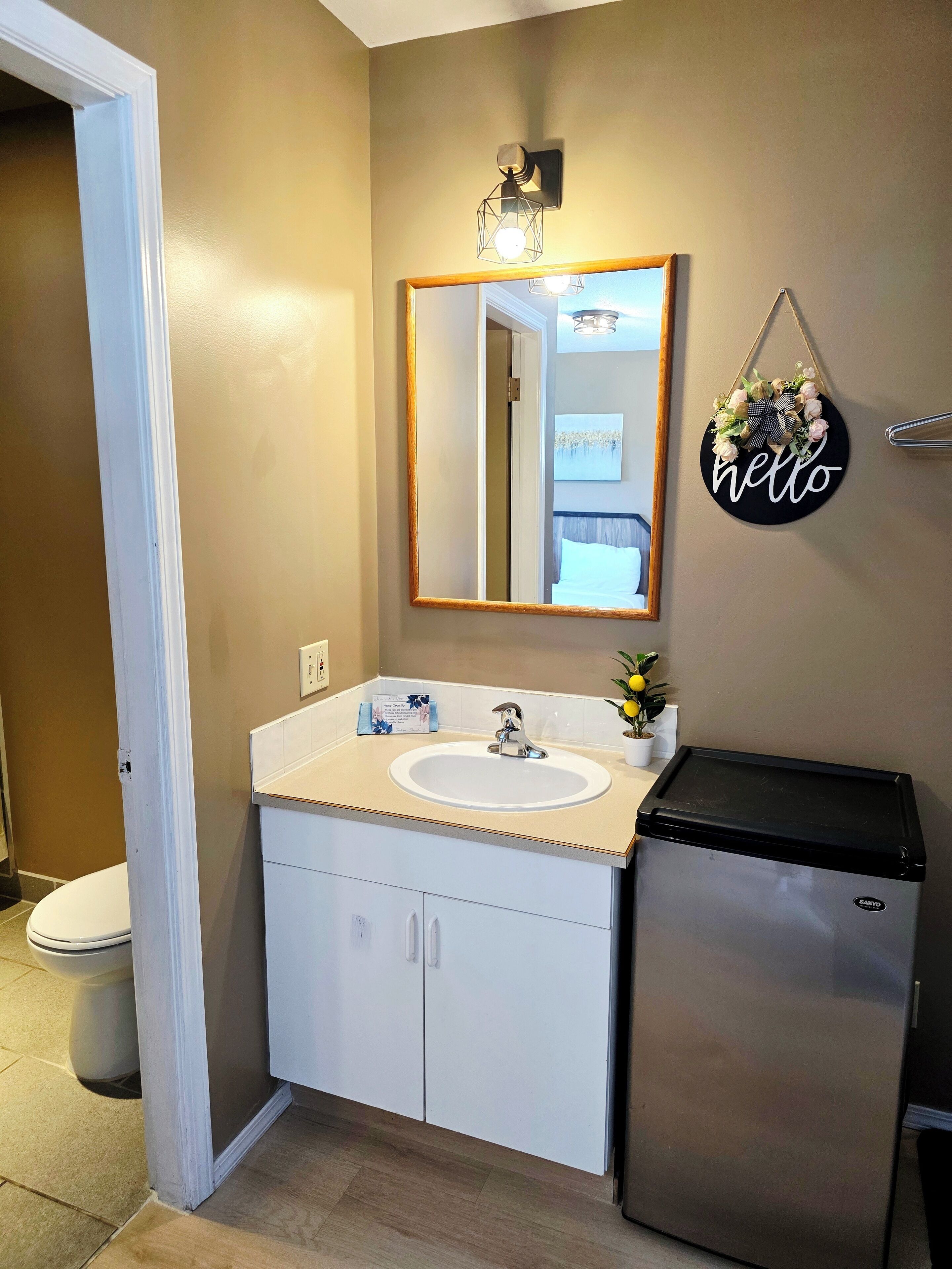 Een badkamer met een wit wastafelmeubel, spiegel, toilet en een kleine koelkast.