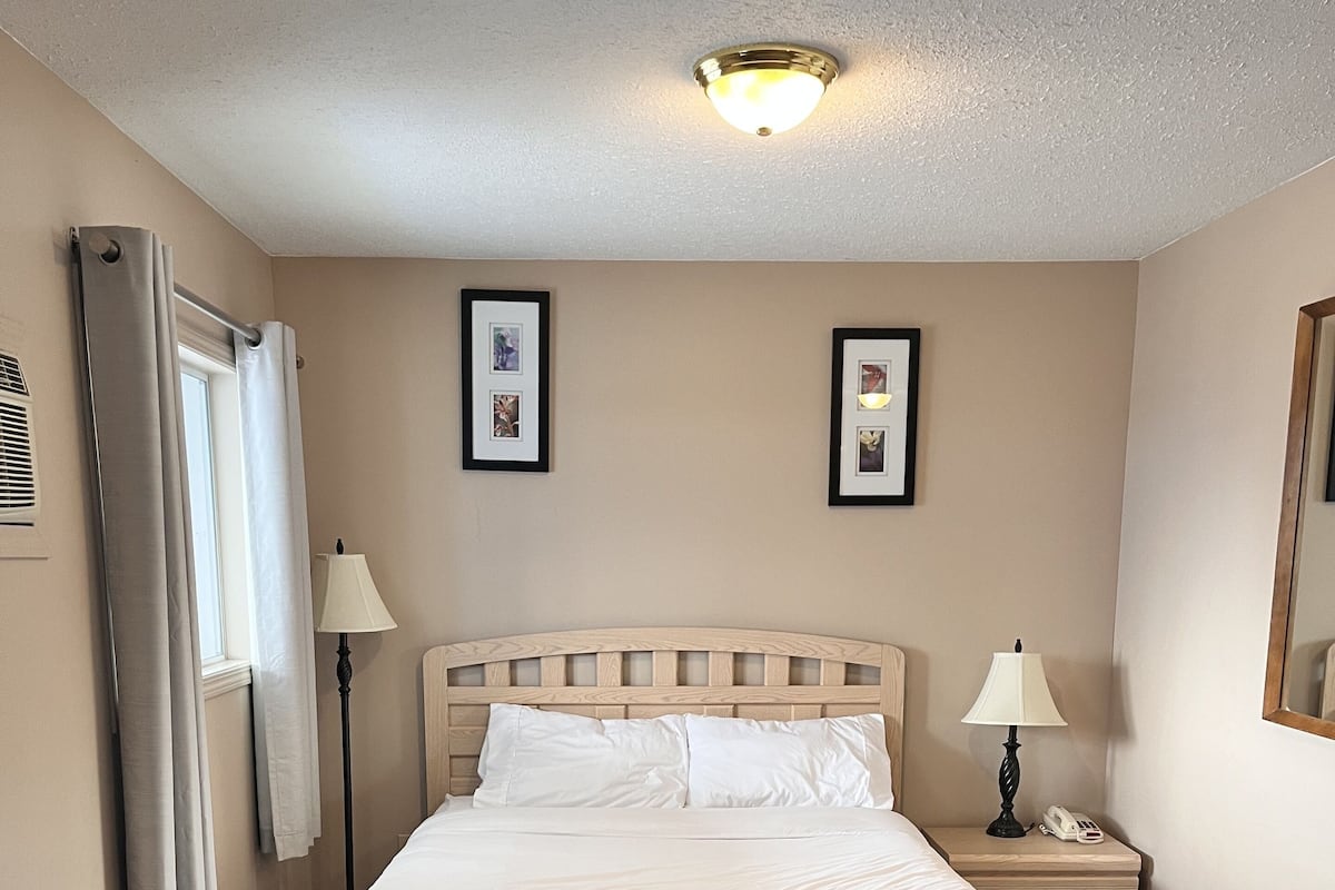 Quarto de hotel com cama, mesas de cabeceira, uma cadeira e uma pequena mesa.