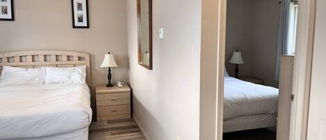 A hotel room with two beds, a wooden headboard, a bedside table with a lamp, and a mirror.