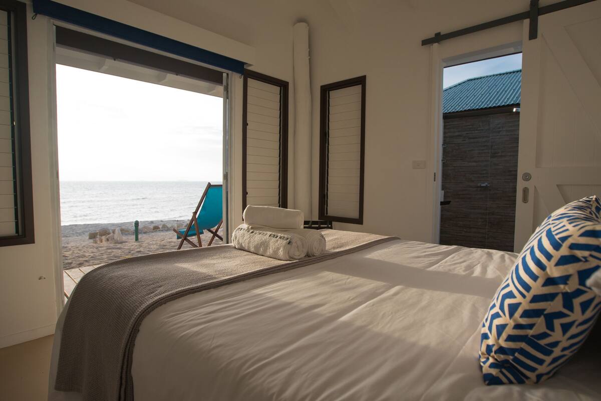 A bedroom with a large bed, a view of the beach, and a chair by the window.