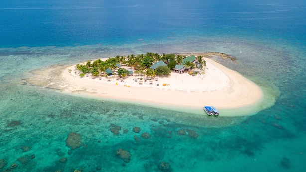 An aerial view of a small island with a beach, clear turquoise waters, and scattered rocks.