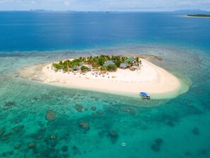 An aerial view of a small island with a beach, clear turquoise waters, and scattered rocks. - South Sea Island (South Sea Island)