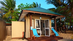 A small beach house with a covered porch, two blue lounge chairs, and a sandy beach area.