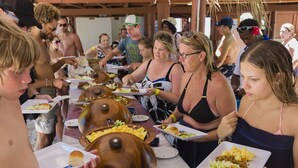 A group of people dining at an outdoor event with wooden food containers and a covered area.