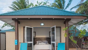 A beachside bungalow with a single bedroom, a balcony, and a sandy ground.