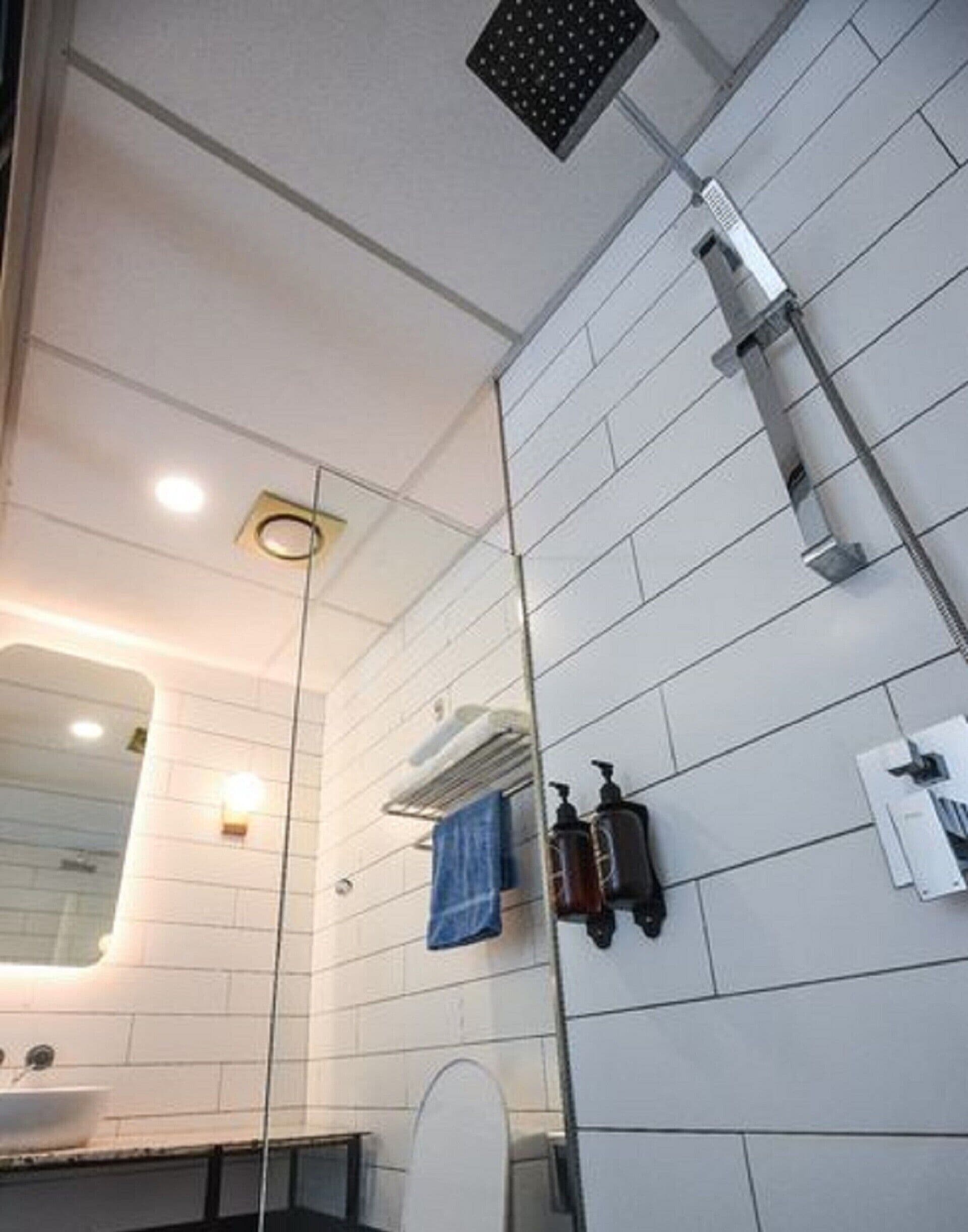 A modern bathroom with a white tiled wall, a glass shower enclosure, a white sink, and a mirror.