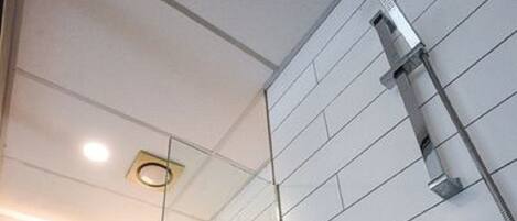 A modern bathroom with a white tiled wall, a glass shower enclosure, a white sink, and a mirror.