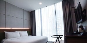 Ein modernes Hotelzimmer mit einem großen Bett, einem kleinen runden Tisch, einem Fernseher und einer Kaffeemaschine.