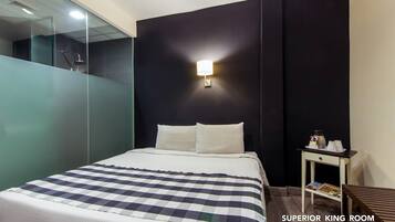 A hotel room with a bed, a nightstand, a wall-mounted lamp, and a glass partition.