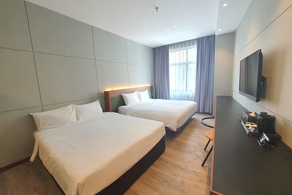 Habitación de hotel con dos camas, un televisor de pantalla plana, un escritorio y una ventana con cortinas.