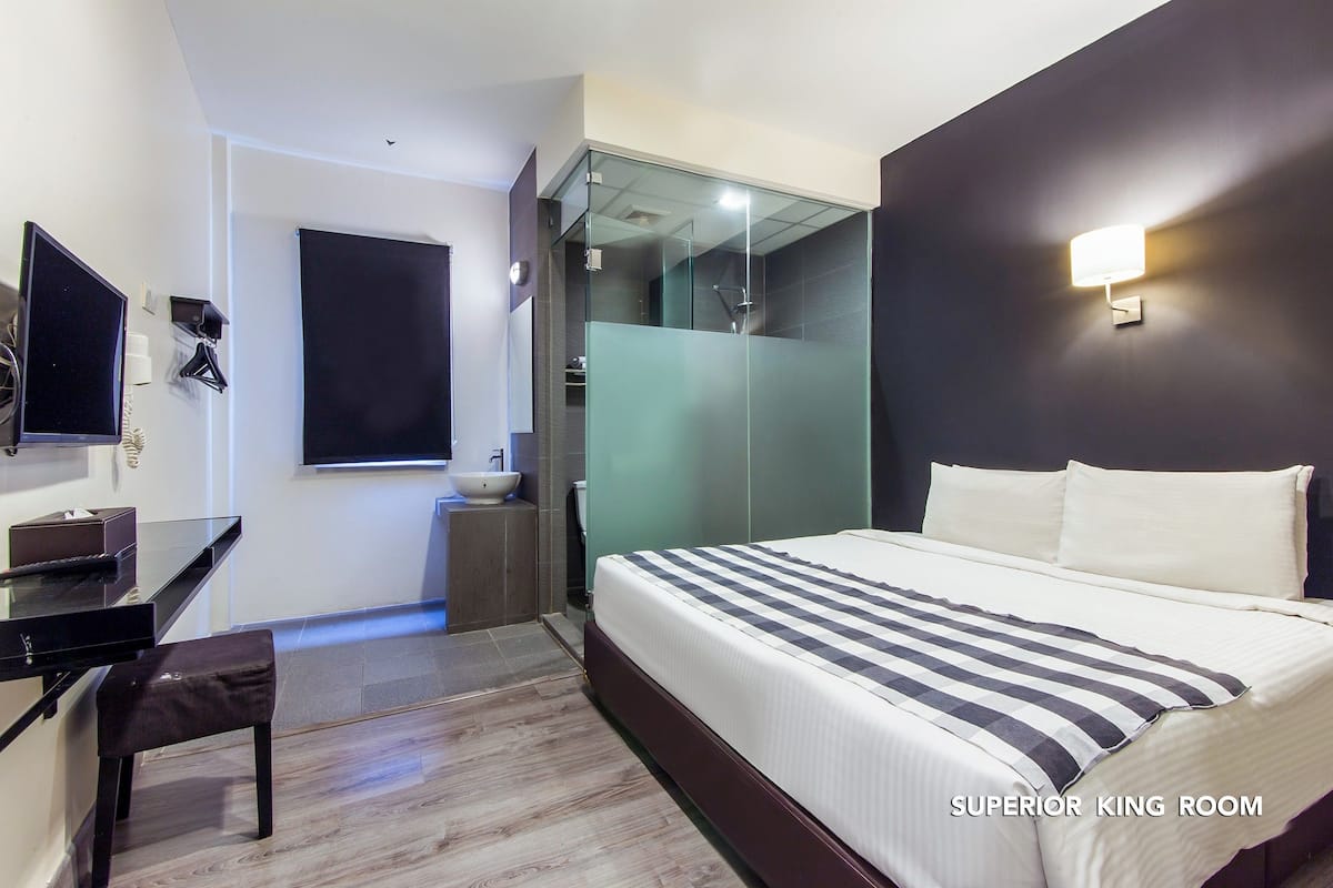 Una habitación de hotel moderna con una cama grande, un escritorio, una silla, un televisor y un baño con mampara de vidrio.