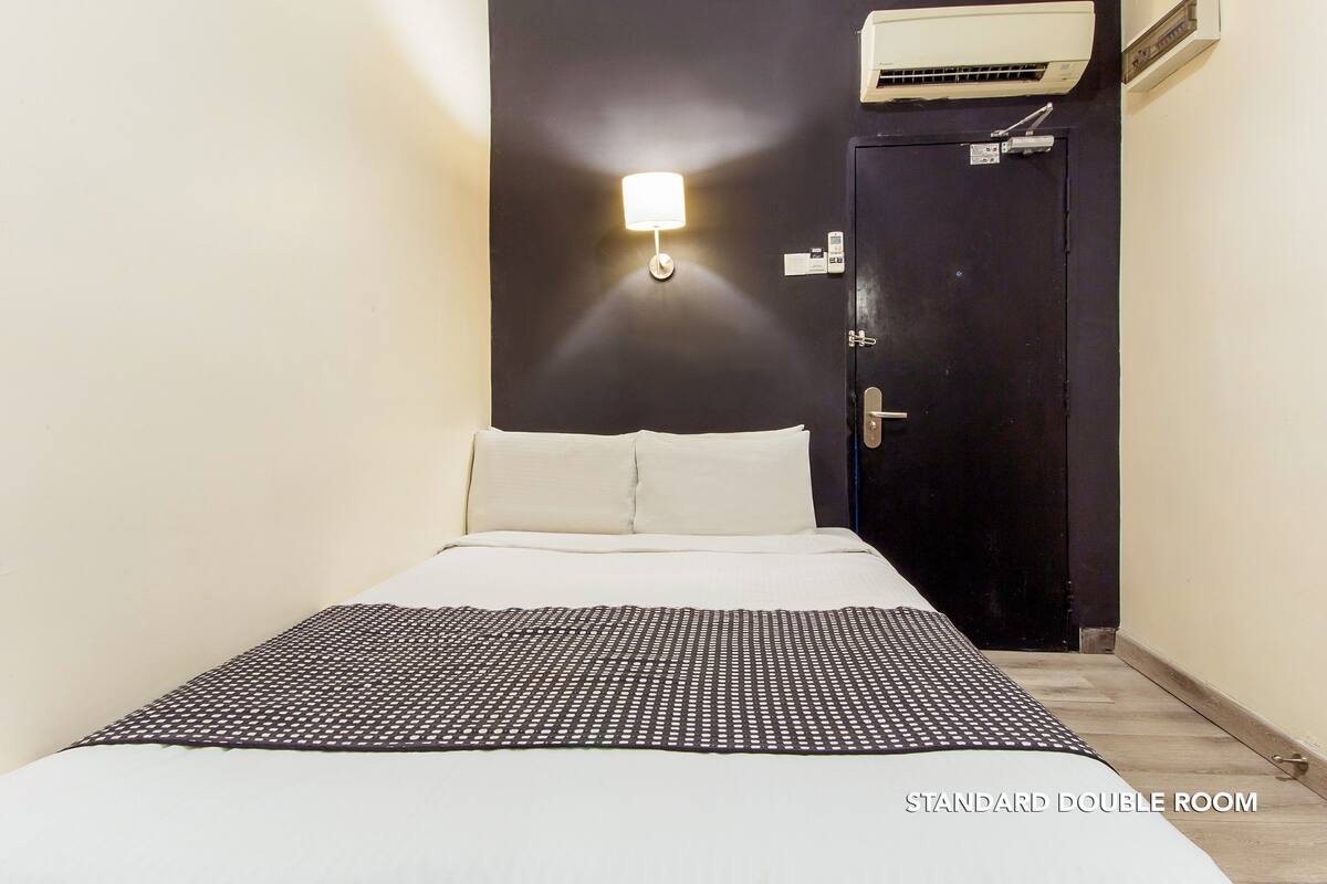 Una habitación doble estándar con una cama, una lámpara de pared, un equipo de aire acondicionado y una puerta.