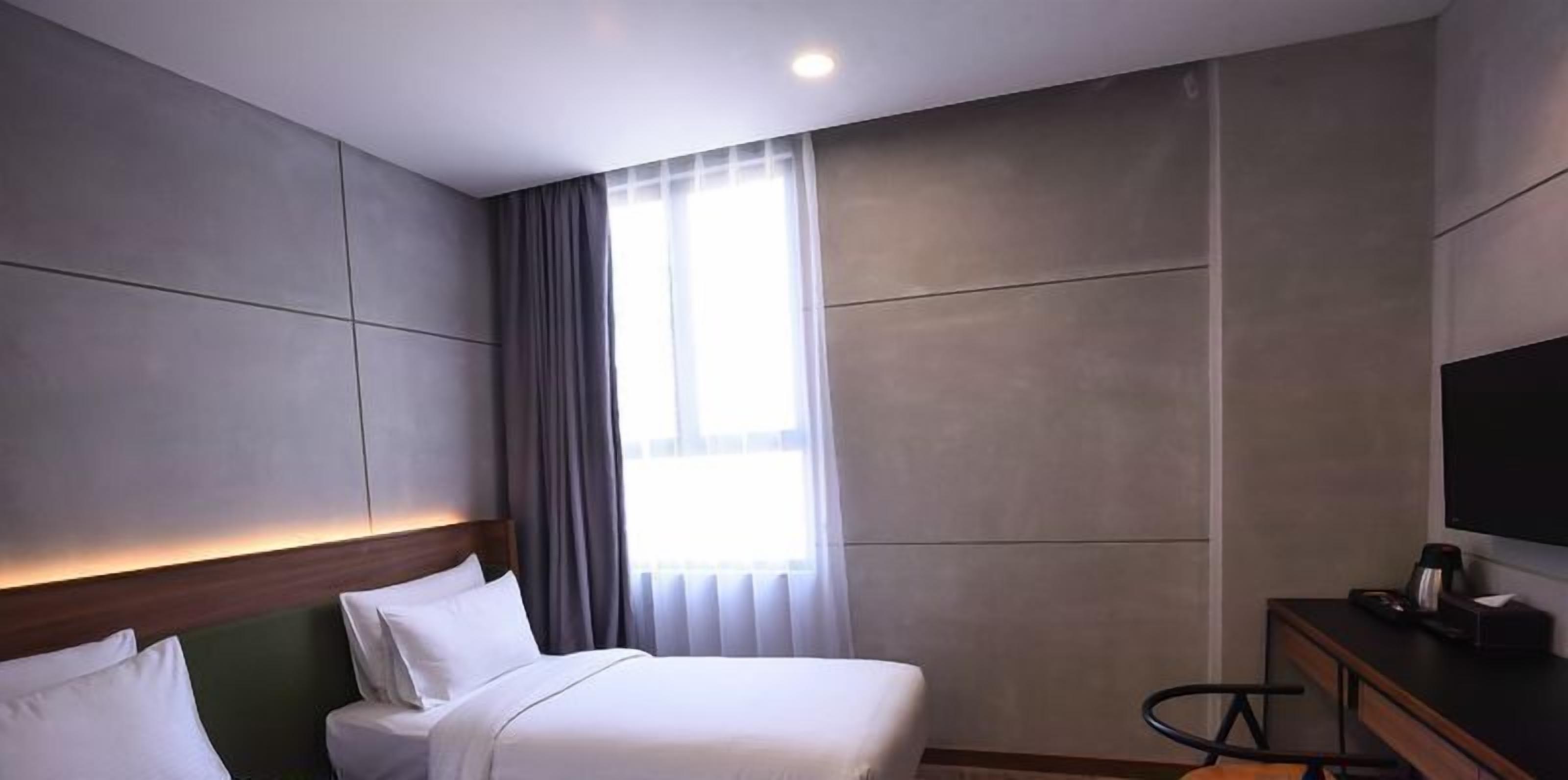 Una habitación de hotel con cama, escritorio con televisor y ventana con cortinas.