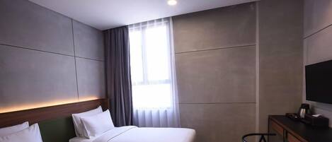 Una habitación de hotel con cama, escritorio con televisor y ventana con cortinas.