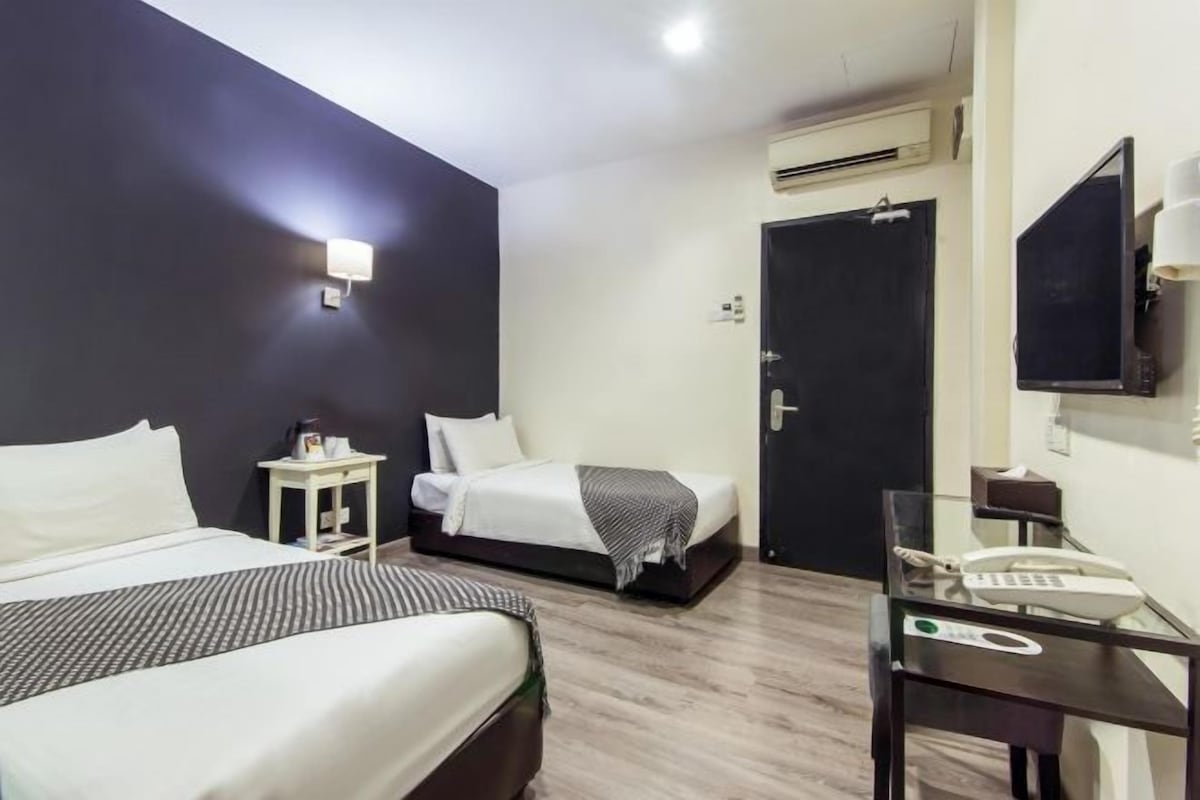 Une chambre d’hôtel avec deux lits, un bureau avec un téléphone, un miroir et un appareil de climatisation fixé au mur.