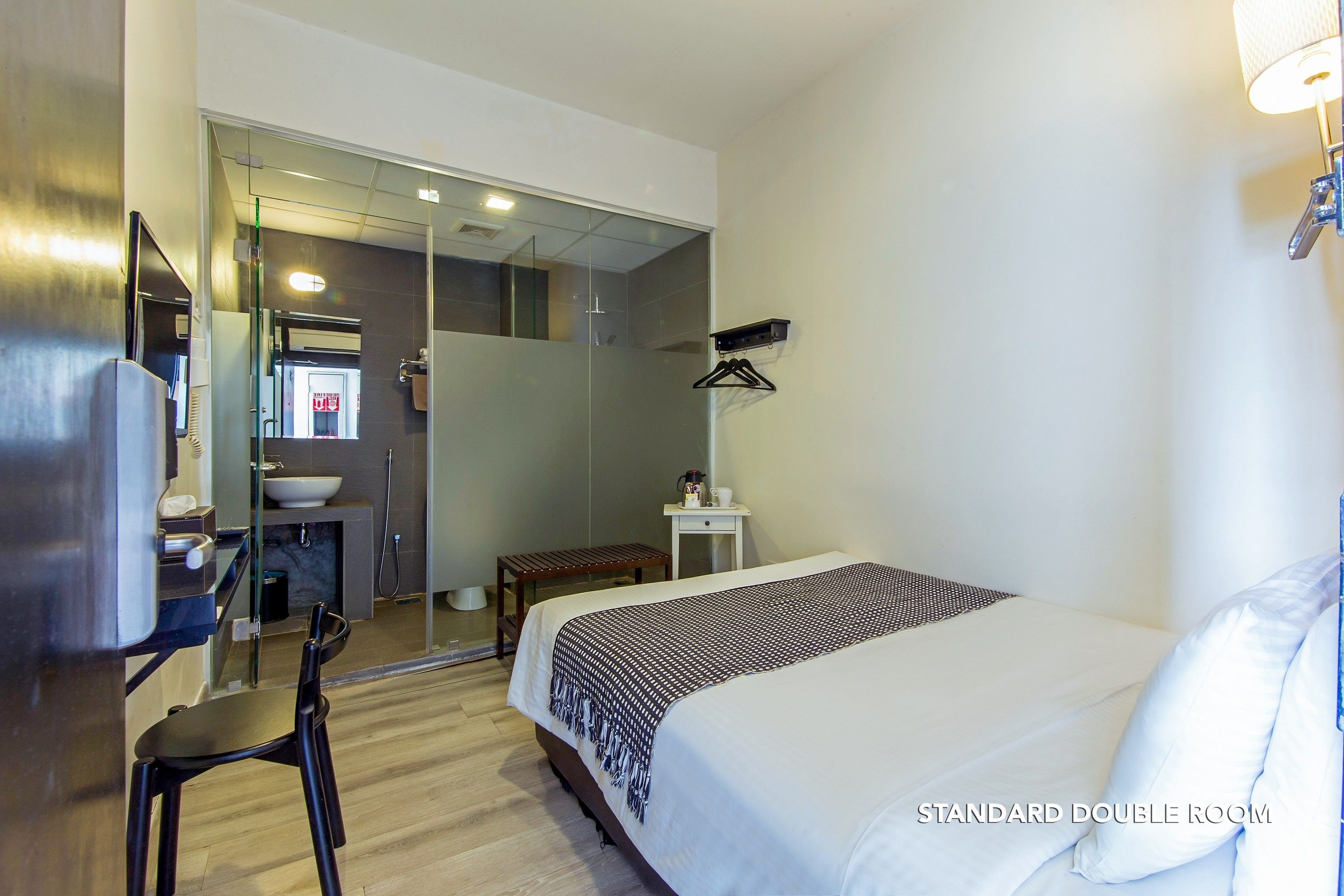 Una habitación doble estándar con cama, mesita de noche, silla y un escritorio pequeño con espejo.