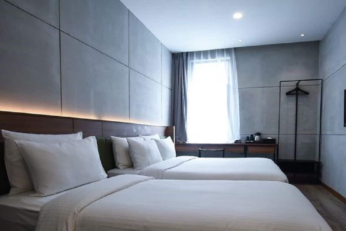 Habitación de hotel con dos camas, un televisor de pantalla plana montado en la pared, una mesita de noche y una ventana con cortinas.