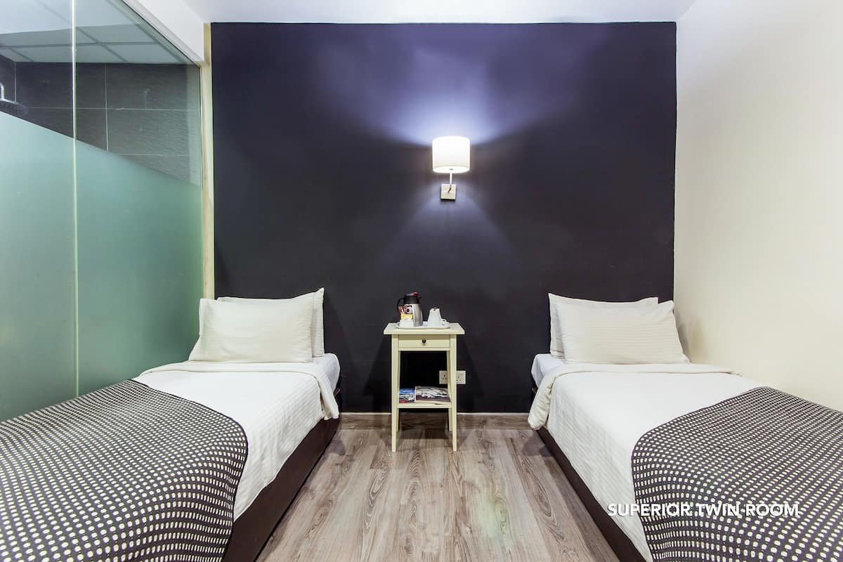 Habitación doble con dos camas, una mesita con lámpara y una pared decorativa oscura.