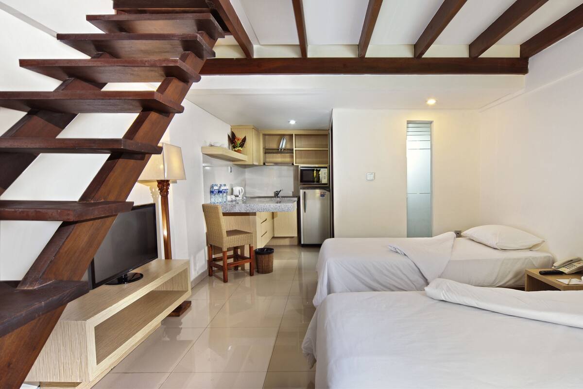 A bedroom with two beds, a TV, and a kitchen area with a refrigerator and microwave.