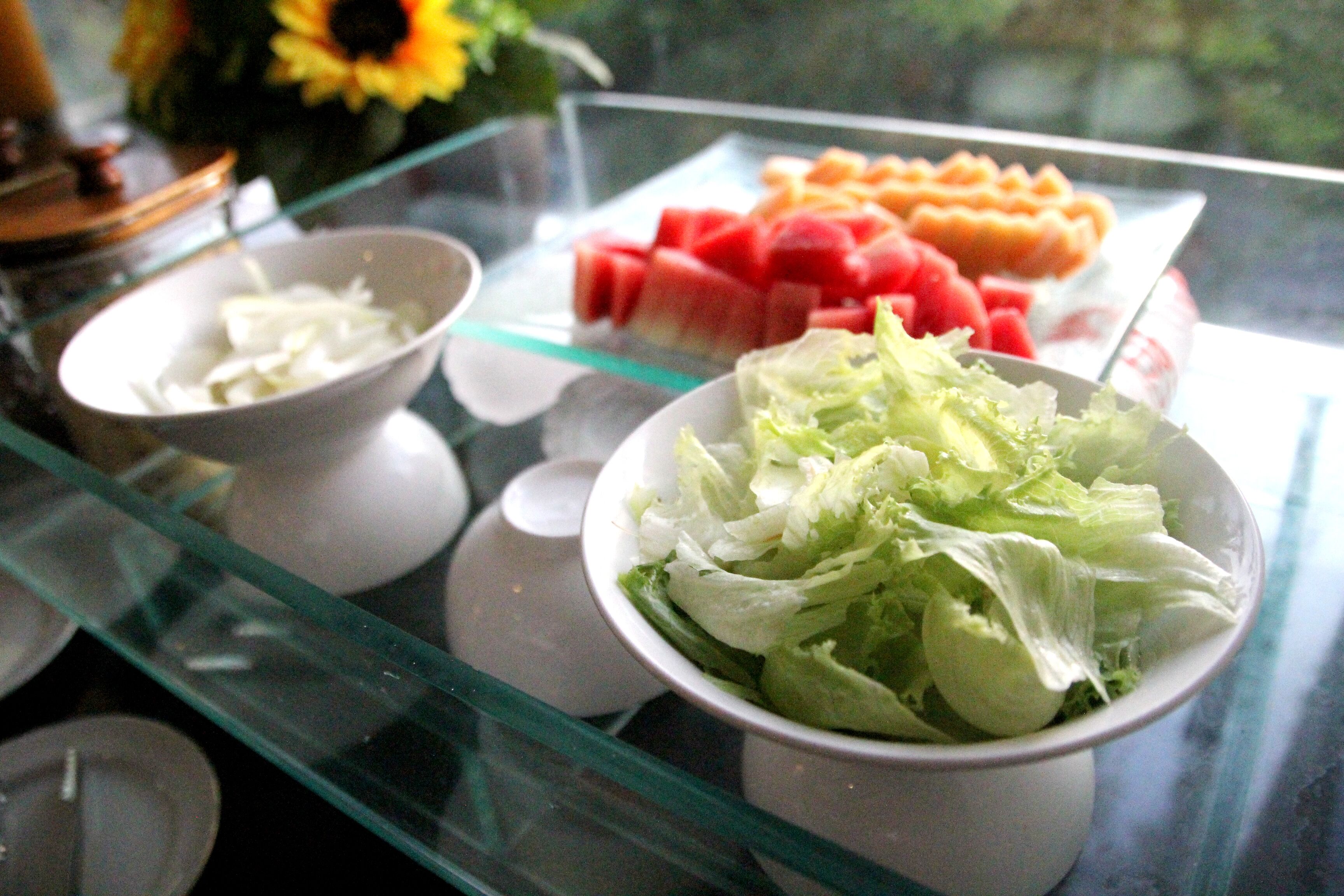 A buffet table with various food items including a bowl of shredded vegetables, a plate of watermelon, and a bowl of lettuce.