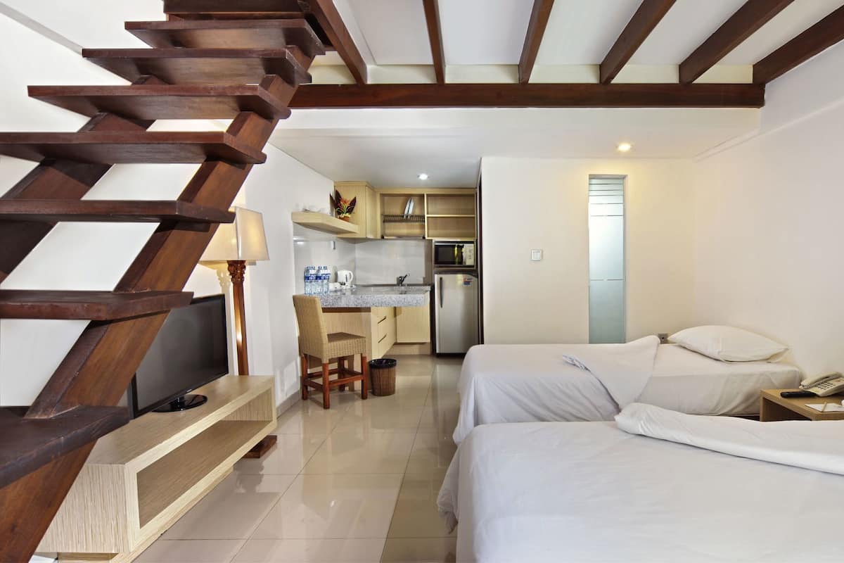 A hotel room with a wooden staircase, a kitchenette, a dining area, and a bed.