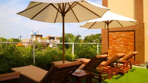 Une terrasse sur le toit, dotée de chaises longues et de parasols, un mur en briques et une vue sur le paysage urbain.
