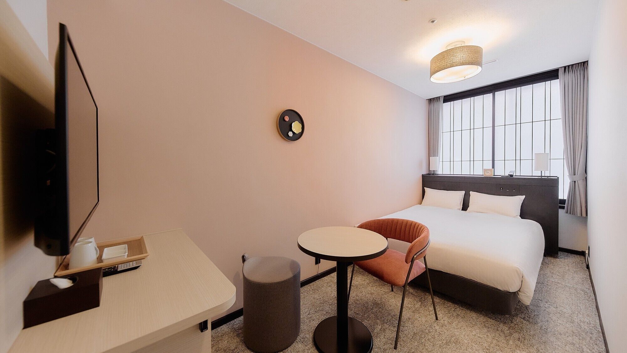 Hotellihuone, jossa on sänky, työpöytä, tuoli, televisio ja ikkuna, jossa on verhot.