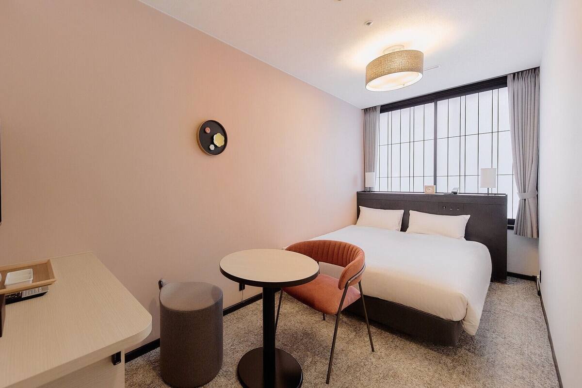 A hotel room with a bed, a desk, a chair, a TV, and a window with curtains.