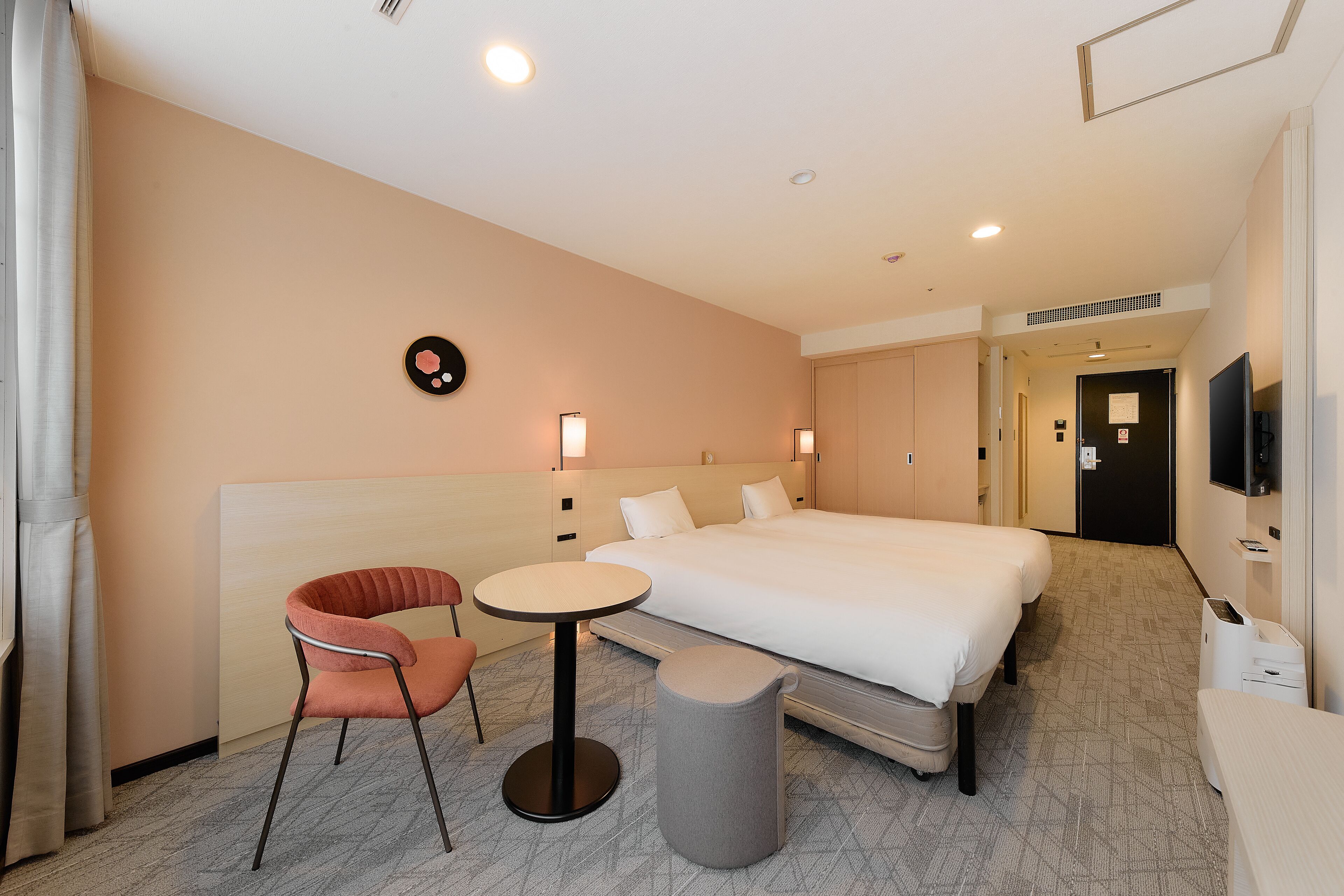 A hotel room with a bed, a chair, a small table, a trash bin, and a television.