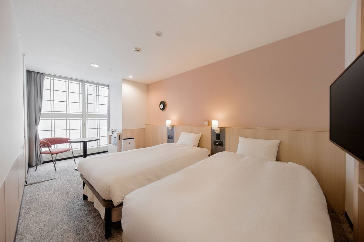 A hotel room with two beds, a desk, a chair, a TV, and a large window.