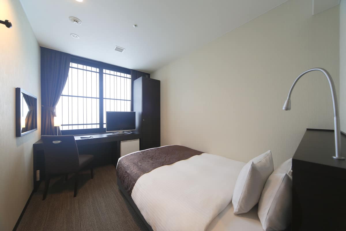 A hotel room with a bed, a desk, a chair, a television, and a window with curtains.