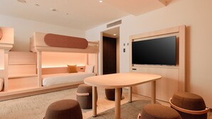 A modern hotel room with a bunk bed, a flat-screen TV mounted on the wall, a round table, and two ottomans. - Kyoto Tower Hotel (Kyoto)