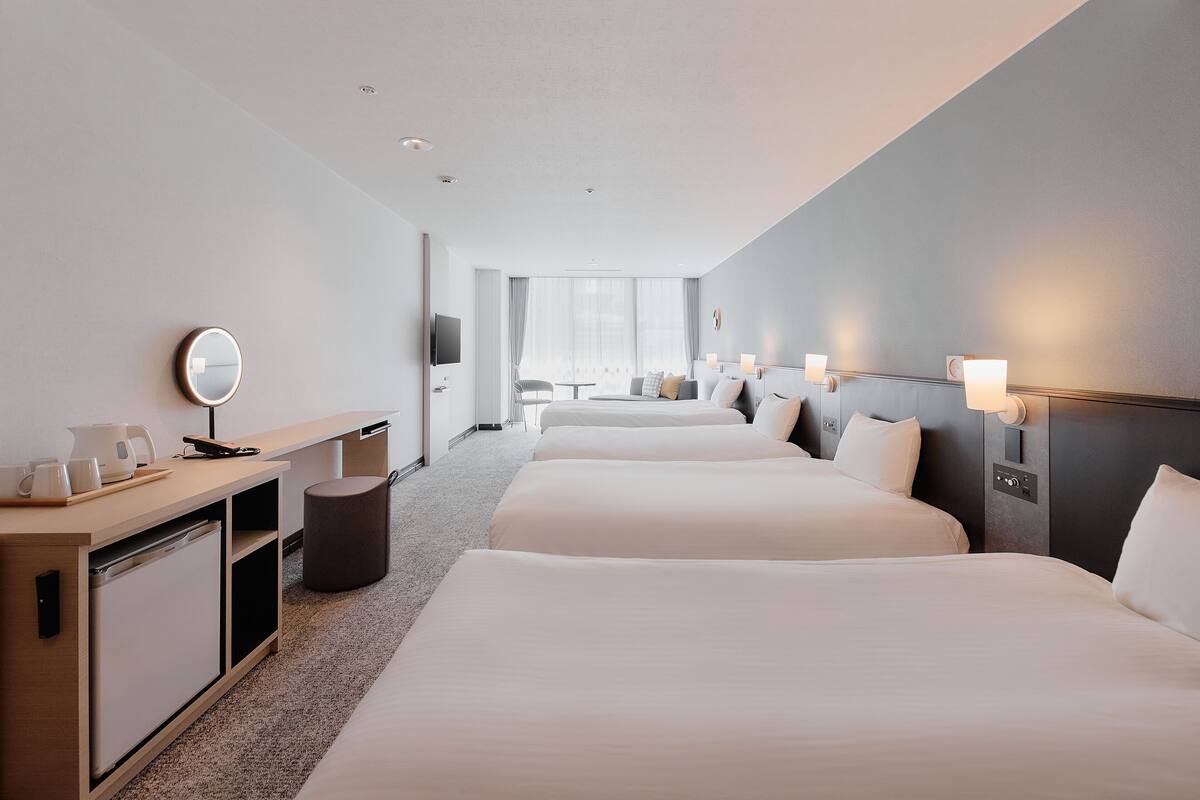 A hotel room with two beds, a desk with a mirror, a TV, and a window with curtains.