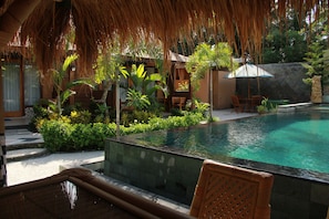 A pool area with a thatched roof, seating, and lush greenery.