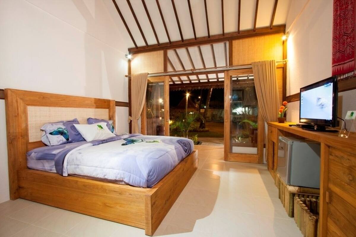 A bedroom with a wooden bed, a television, and a sliding glass door leading to an outdoor area.