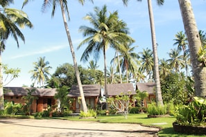 A tropical resort with thatched-roof cottages surrounded by palm trees and lush greenery. - Green Asri (Senggigi)