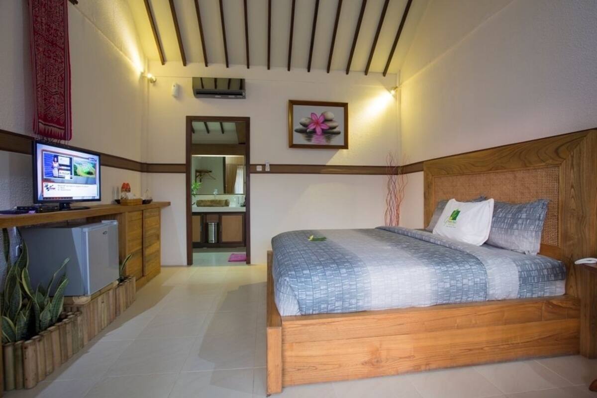 A bedroom with a wooden bed, a desk with a computer, a small refrigerator, and a mirror.