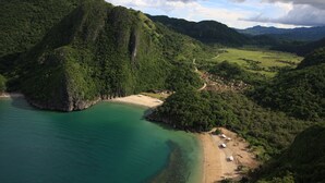 Un paisaje costero con una playa, un pequeño asentamiento y colinas verdes exuberantes.
