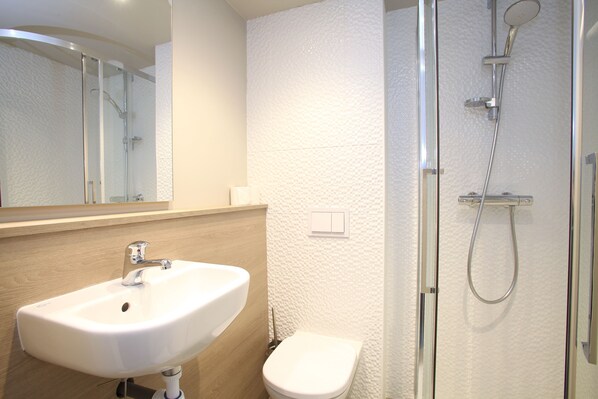 A modern bathroom with a white sink, toilet, and glass shower enclosure.