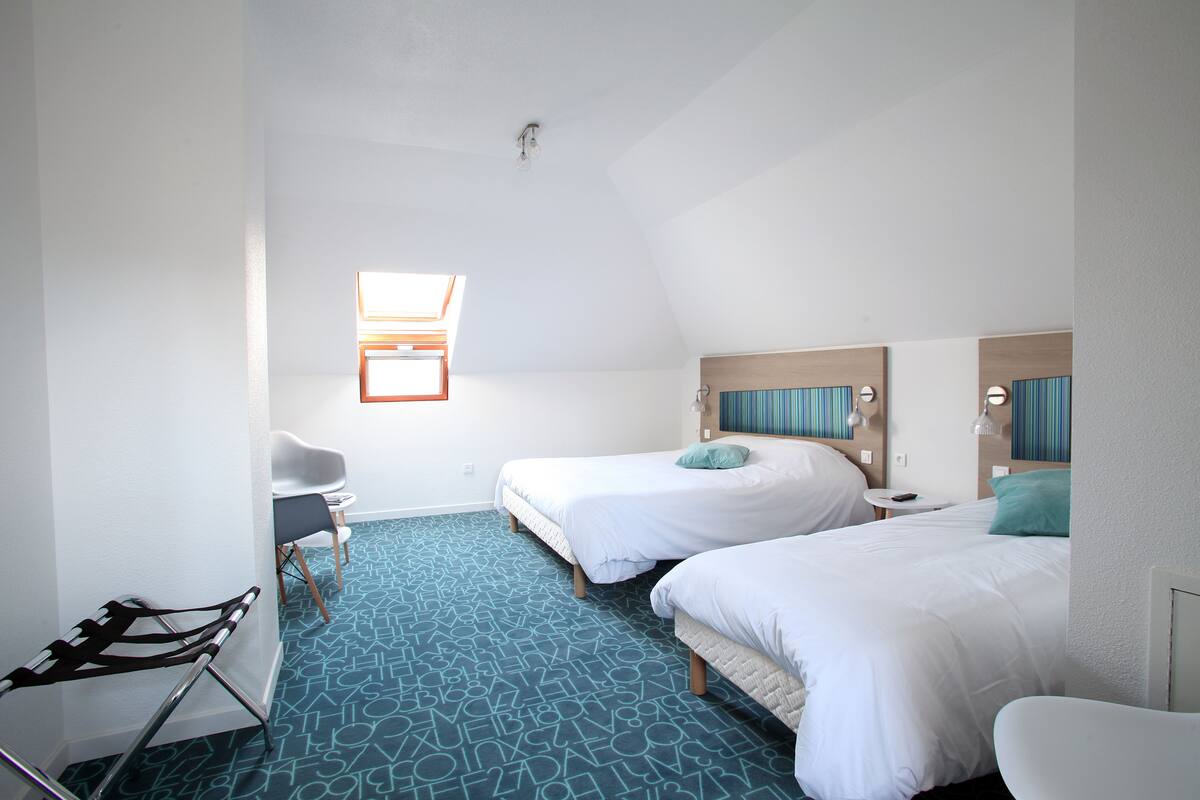 Une chambre d’hôtel avec deux lits, un bureau, une chaise et une petite fenêtre.