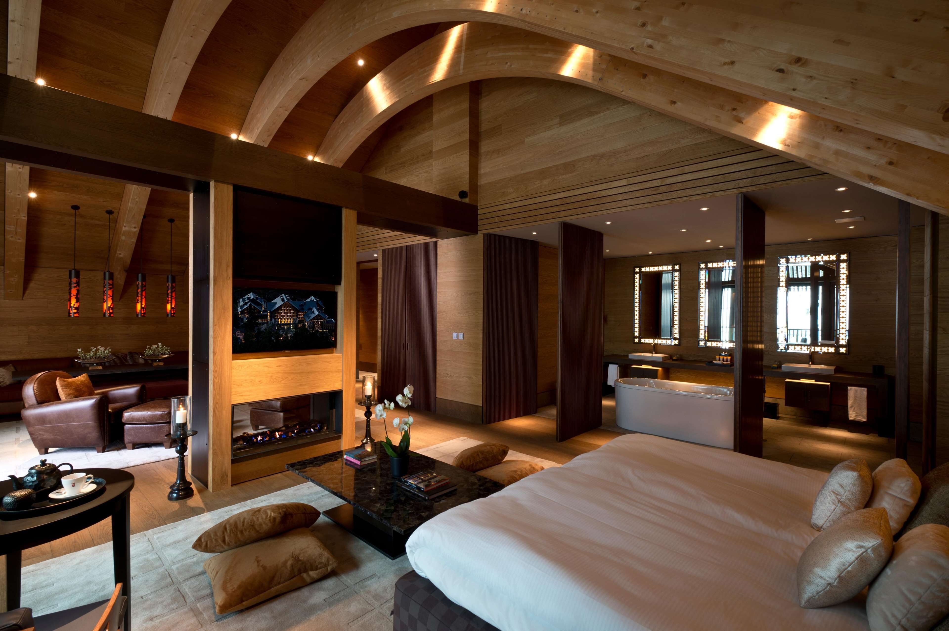 A spacious bedroom with a large bed, a sitting area with a fireplace, and a separate bathroom with a vanity and mirror.