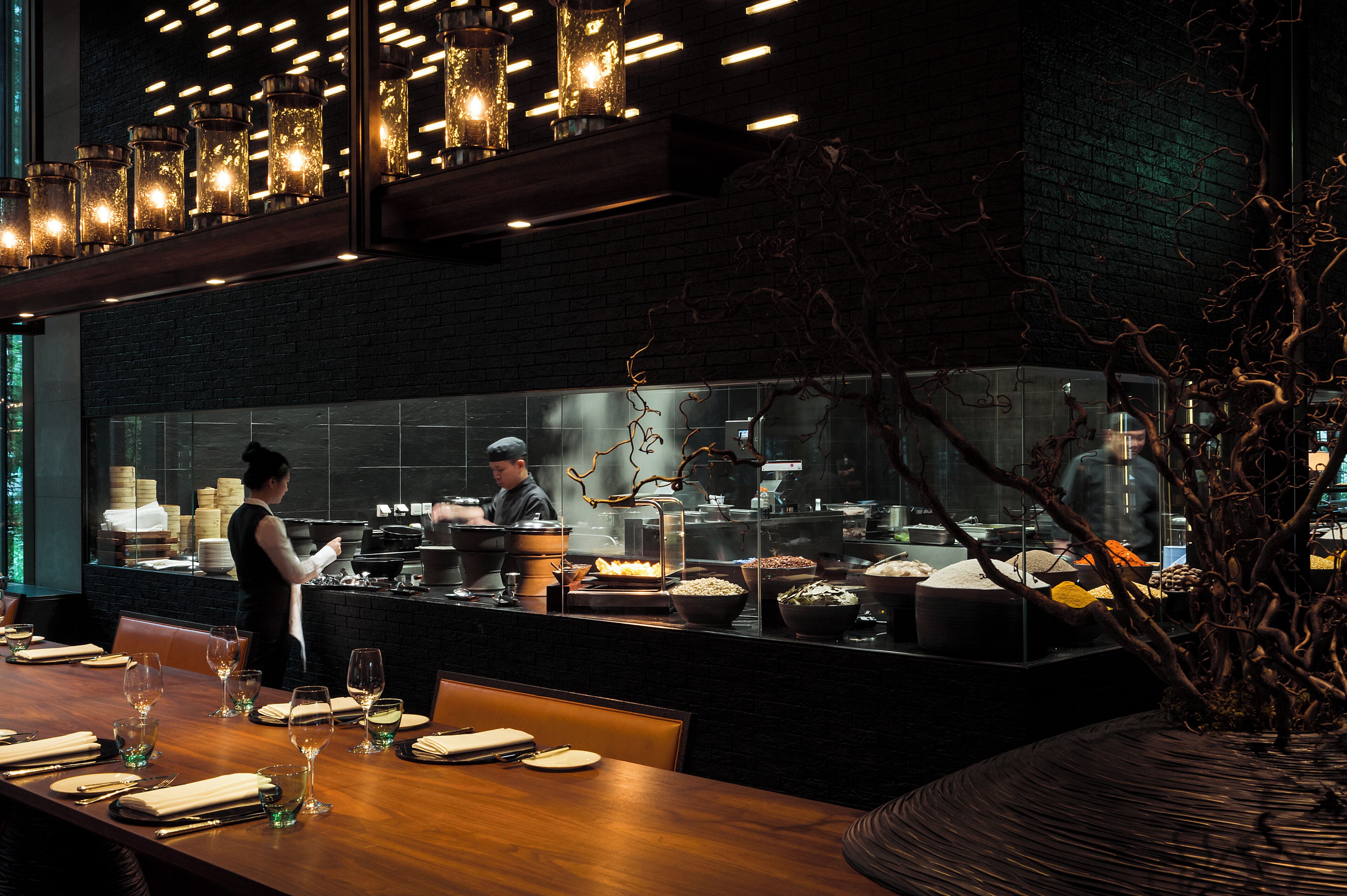 A restaurant with a long counter, a chef preparing food, and a dining area with tables set for guests.
