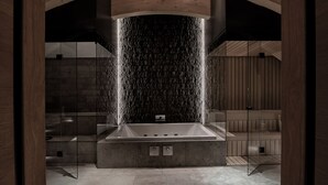 A modern bathroom with a freestanding bathtub, a marble wall, and wooden beams. - The Chedi Andermatt (Andermatt)