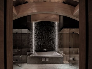 A modern bathroom with a freestanding bathtub, a stone waterfall feature, and wooden beams. - The Chedi Andermatt (Andermatt)