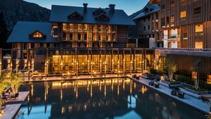 A modern hotel with a large pool, outdoor seating, and a mountain backdrop. - The Chedi Andermatt (Andermatt)