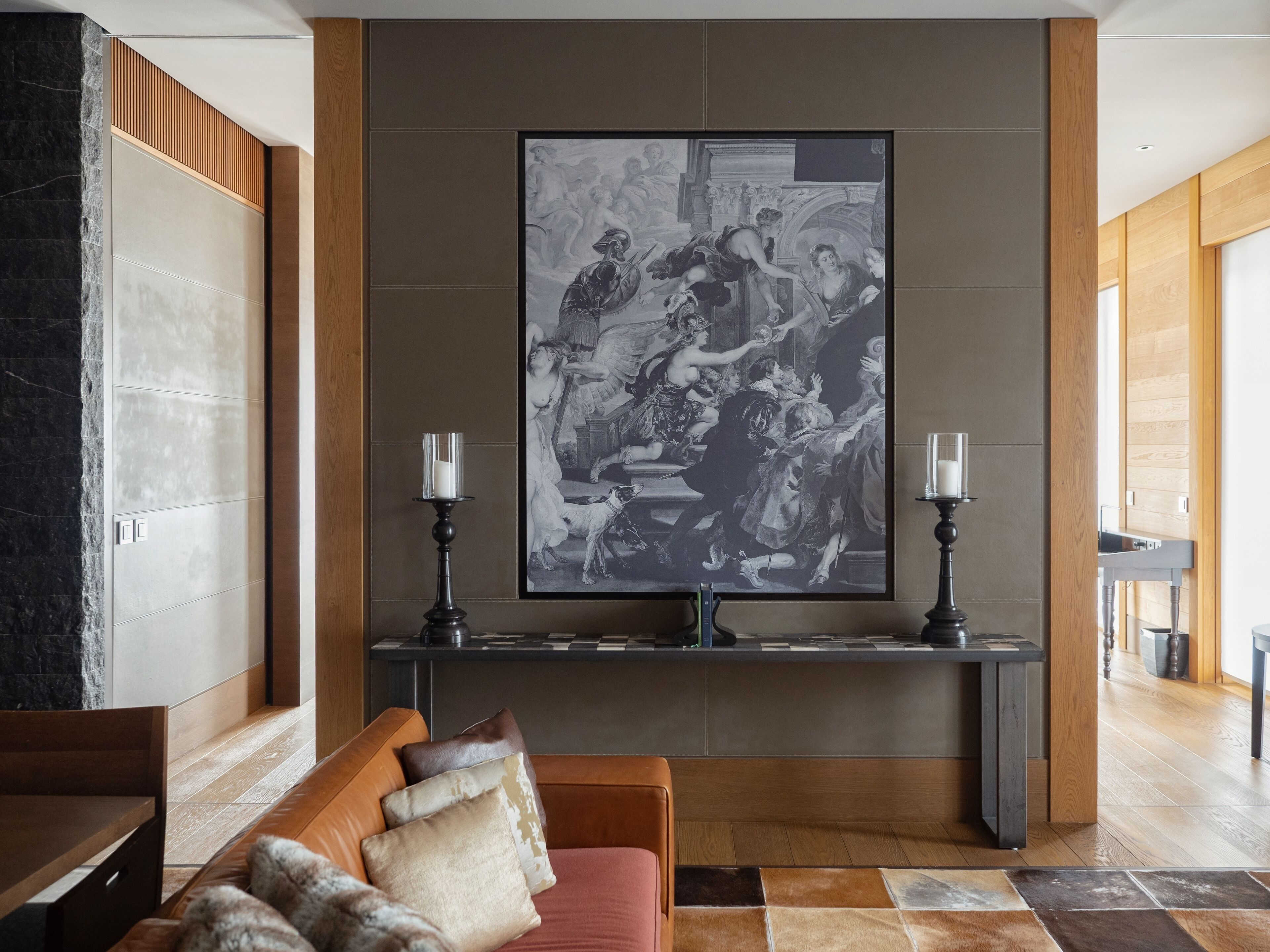 A modern lobby with a large black and white painting, a wooden bench, and a console table with two candles.
