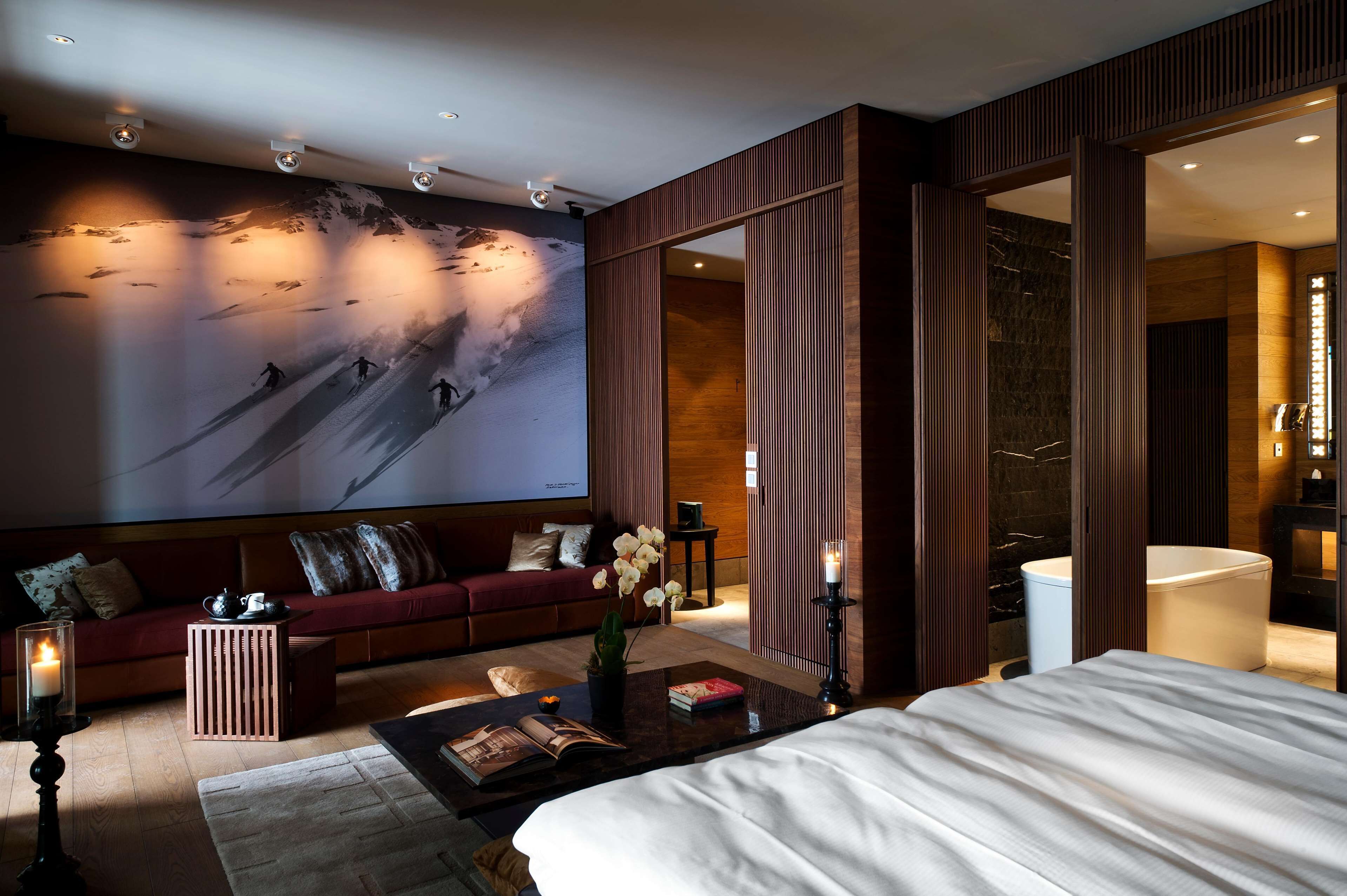 A modern hotel room with a large wall mural, a sofa, a bed, a coffee table, and a bathroom visible through an open door.